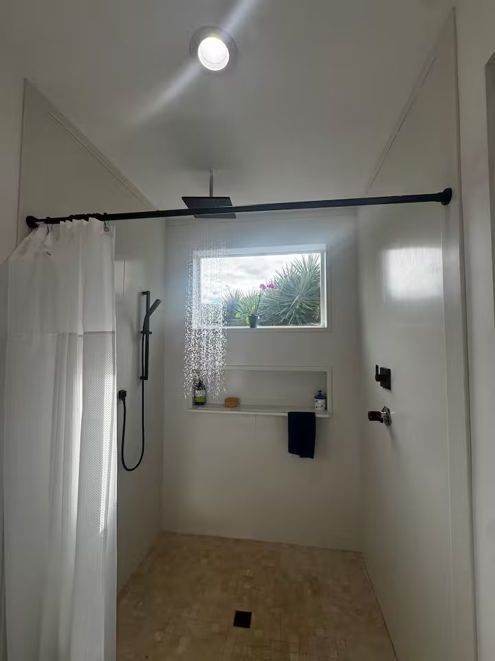 Walk-in shower with matte black rainfall fixture and a window looking onto an agave plant