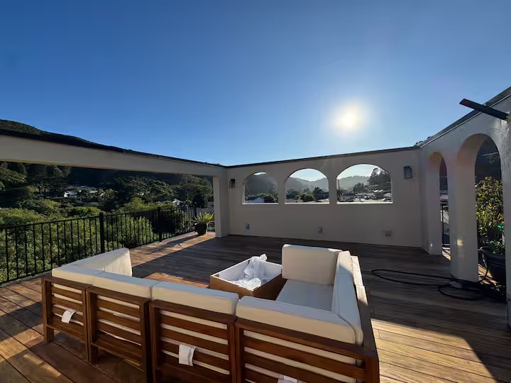 Rooftop deck in daylight with cushioned wood sofas, stucco arches, and Pacifica hills beyond