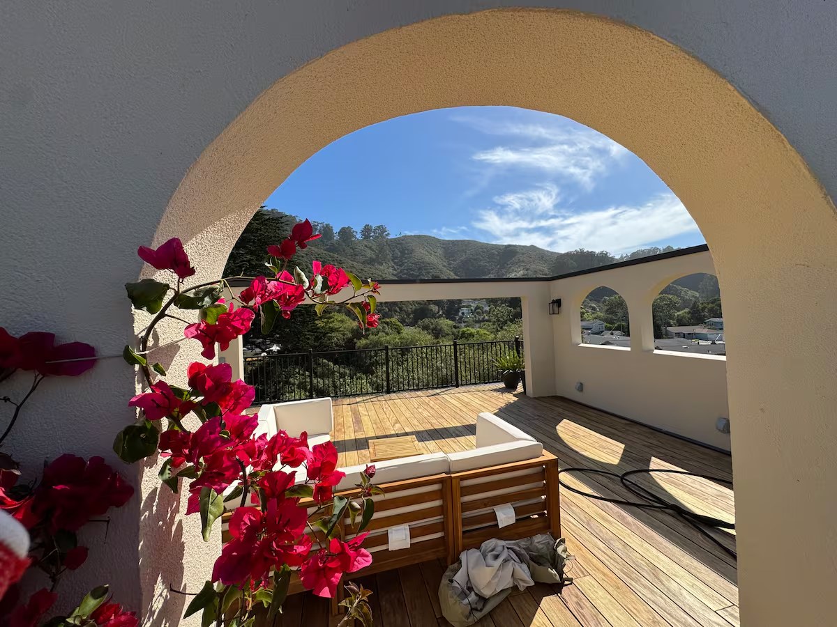 Rooftop stucco arch draped with pink bougainvillea framing the mountains