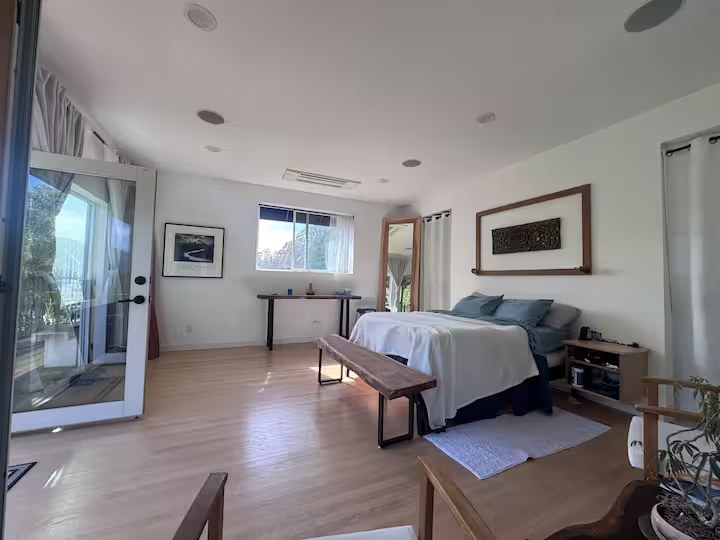 Master suite with king bed, wood floors, framed art, and French doors opening onto a private balcony